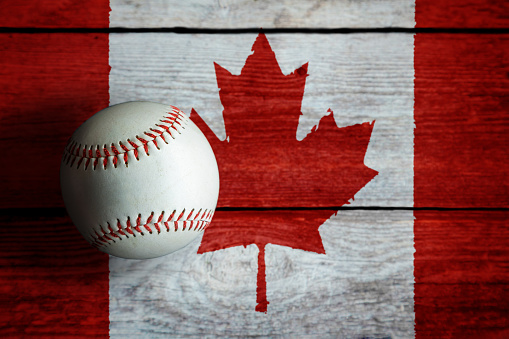 Leather baseball on rustic wooden background painted with Canadian flag with copy space. Canada is one of the top baseball nations in the world.