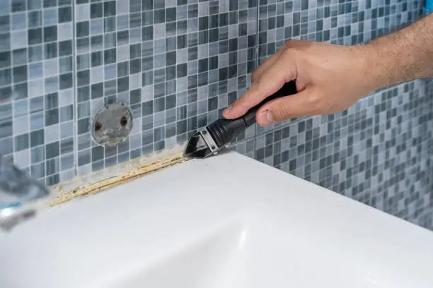 Photo of Plumber removes old dirty silicone from tub, cuts silicone adhesive with cutter