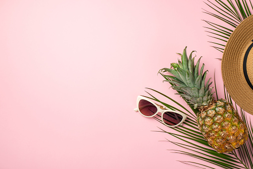 Summer vacation concept. Top view photo of pineapple headwear sunglasses and palm leaves on isolated pastel pink background with copyspace