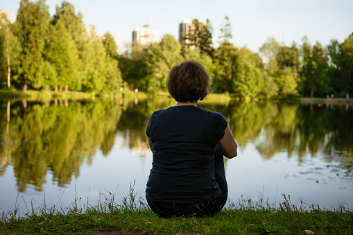 adult woman sitting by the lake turned her back, loneliness concept