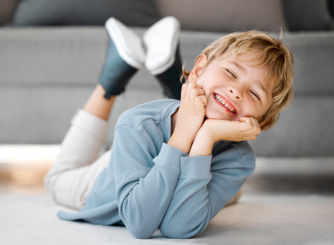Portrait of a happy boy child looking and smiling at the camera with dental teeth showing. Adorable caucasian kid lying on the floor and relaxing at home. For a healthy mouth and gums, start young