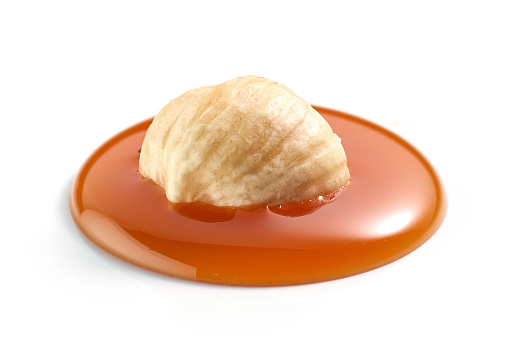 hazelnut in melted caramel drop isolatedd on white background