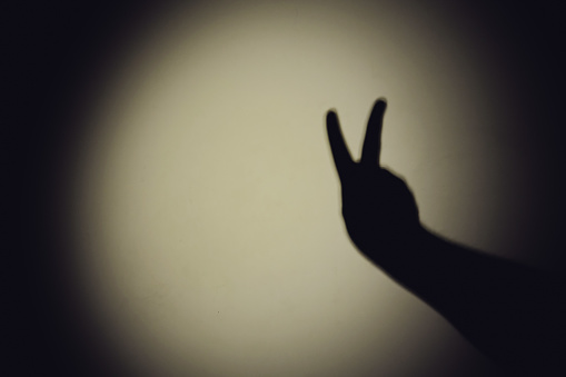 Shadow of a hand from the night light of a flashlight on a white wall. Dark silhouette of a man hands from the light of a lamp