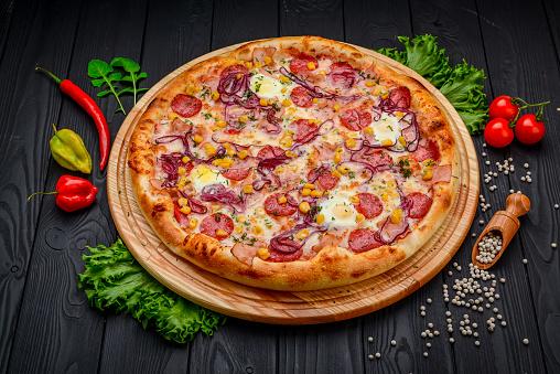 Serving delicious pizza with quail eggs, ham, sausage and vegetables on a black background
