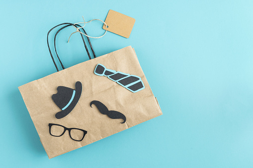 Brown paper bag with decoration of motifs in black color referring to father's day on blue background. Father's day concept. Copy space.