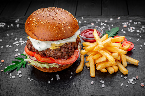 An american burger with fried potatoes on the dark background.