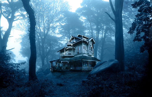 Light emanates from inside a haunted house as a full moon rises on a foggy and misty Halloween night.