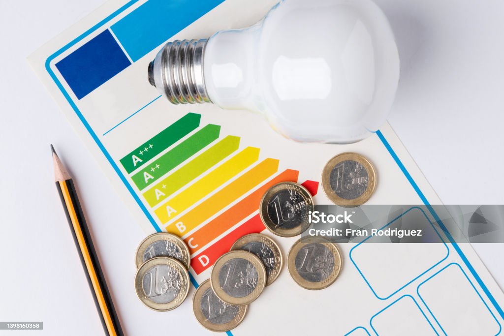 Energy efficiency scale with a light bulb, a pencil to make calculations and coins representing the cost of energy Economy Stock Photo