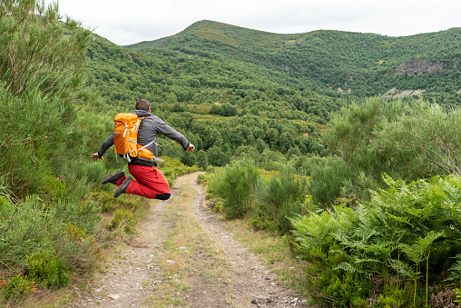 Man jumping while is trekking solo at the mountains. Summer active vacations. Freedom concept.