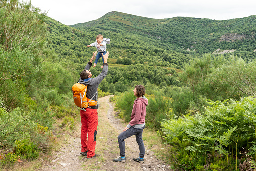 Happy family having fun outdoors in the mountains. Father is throwing his baby girl up in the air while mother is looking at them.