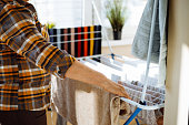 Woman on sunny day standing in home room near clothesline board and hanging clean wet clothing back view closeup. Housewife tidy up house and arranging fresh clothes. House cleaning concept