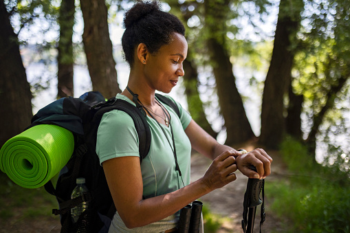 African-American Ethnicity woman checking a heartrate or distance on smartwatch in the forest during a hiking walk