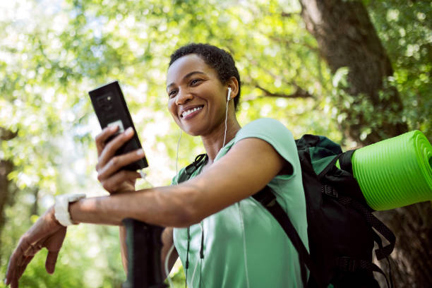 femme afro-américaine souriante dans la forêt utilisant un smartphone - black forest audio photos et images de collection