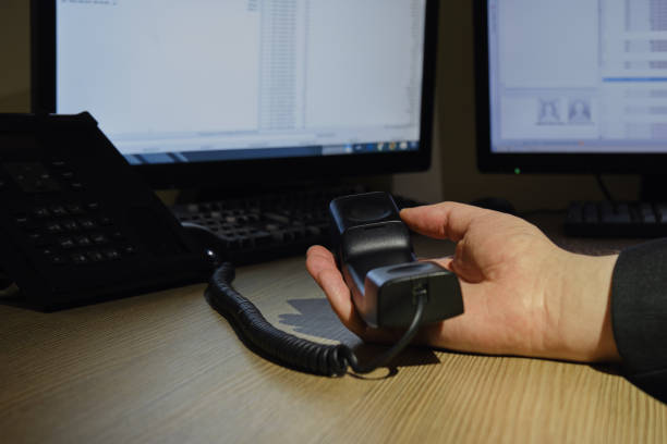 istock A hand holds a landline phone handset on an office desk with computer monitors 1398168025