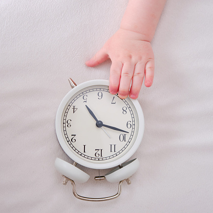 Baby toddler boy holds an alarm clock in his hand. Child with a white alarm clockt, close-up