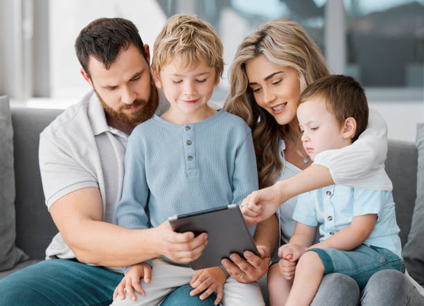 istock Happy relaxed family of four using a digital tablet device while bonding on the sofa together at home. Young couple checking social media and watching a movie with their two cute caucasian sons 1398169823