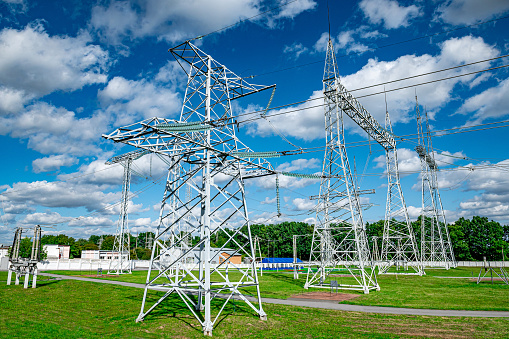 Electrical net of poles on a panorama of blue sky and green meadow.