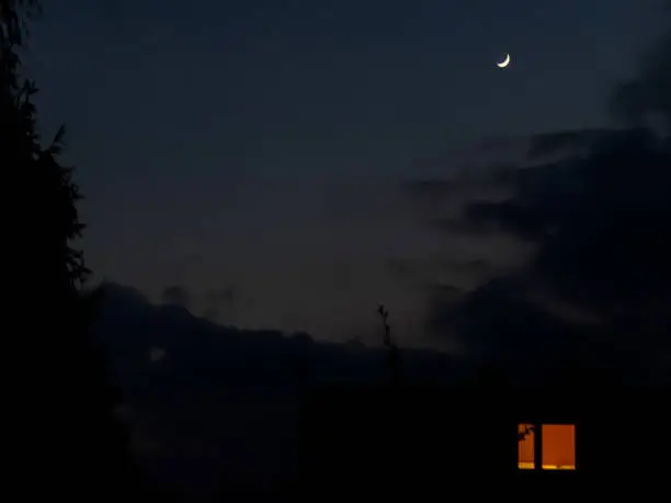 a sickle-shaped moon rising over a partially cloudy evening sky