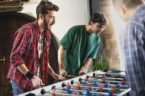 Group of cheerful young people friends playing table football carefree together - concept of happy fellows having fun with recreational activities