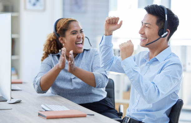 istock Two happy young call centre telemarketing agents clapping and cheering with joy while working together in an office. Excited  african american and asian assistants celebrating successful sales and reaching targets to win 1398177816