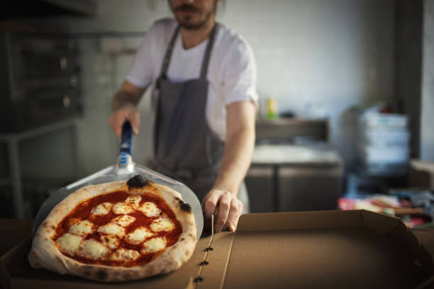 Closeup front view of a mid 30's male chef serving freshly baked pizza into a pizza box.