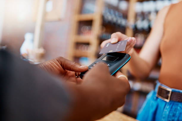 istock Closeup of unknown mixed race customer using a wireless credit card machine to pay for her coffee. African american barista assisting a woman in a cafe. Contactless paying system during covid pandemic 1398179494