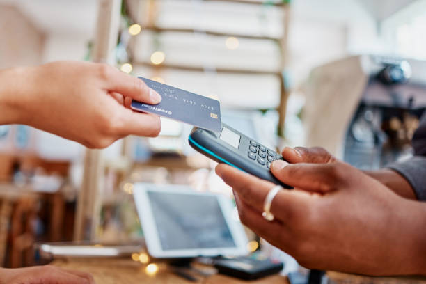istock Closeup of unknown mixed race customer using a wireless credit card machine to pay for her coffee. African american barista assisting a woman in a cafe. Contactless paying system during covid pandemic 1398179500