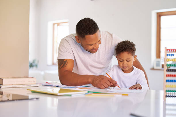 istock Mixed race boy learning and studying in homeschool with dad. Man helping his son with homework and assignments at home. Parent teaching child to colour and write at home during lockdown 1398180354