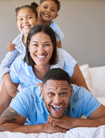 Portrait of a smiling boy and girl lying on their parents in a pile at home. Mixed race couple bonding with their son and daughter. Hispanic siblings enjoying free time with their mother and father
