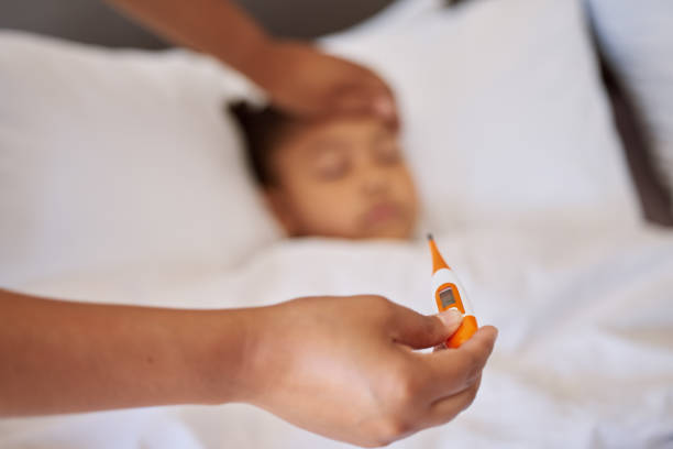 petite fille malade au lit pendant que sa mère utilise un thermomètre pour vérifier sa température. parent métis sentant le front de sa fille. enfant hispanique se sentant malade et dormant pendant que la mère vérifie la fièvre - thermometer cold fever focus photos et images de collection