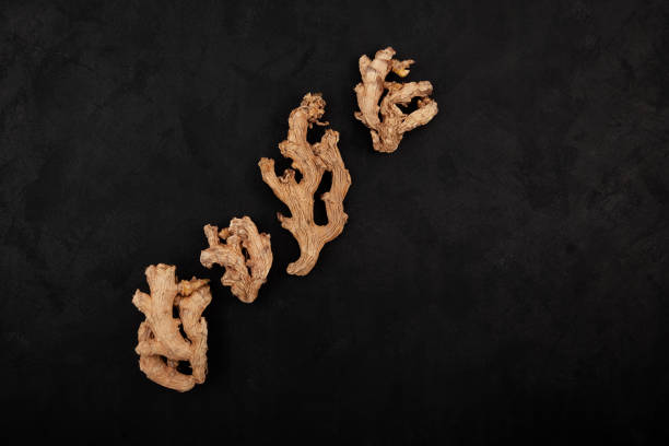 Dried ginger roots on black textured background, top view. Ginger is ground and used as spice in cooking and folk medicine.