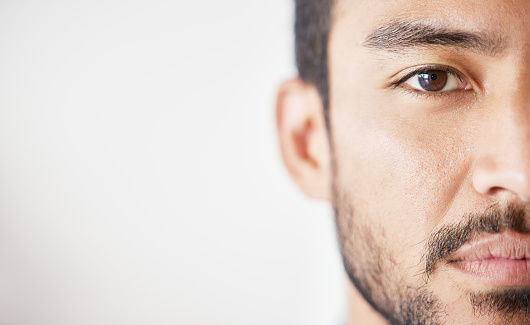 Close up of mixed race male looking serious against a grey background. Asian male standing indoors with no expression and copyspace