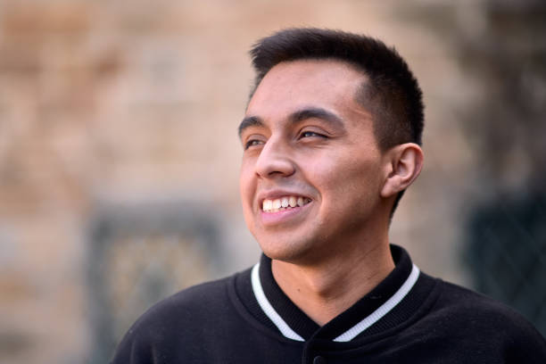 Front view of a young man in black clothes smiling outdoors looking away in selective focus.