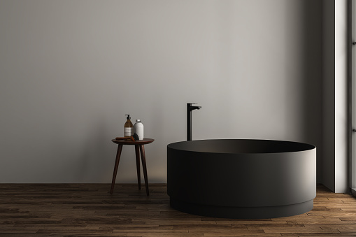 Modern oval black bathtub is standing in front gray wall and stool in empty bathroom. Minimalist concept. 3d rendering