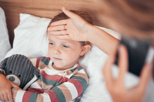 Closeup shot of a cute little caucasian girl looking sick and unwell while lying in bed. Unknown woman feeling her daughters temperature while using a cellphone to call for help Closeup shot of a cute little caucasian girl looking sick and unwell while lying in bed. Unknown woman feeling her daughters temperature while using a cellphone to call for help fever stock pictures, royalty-free photos & images