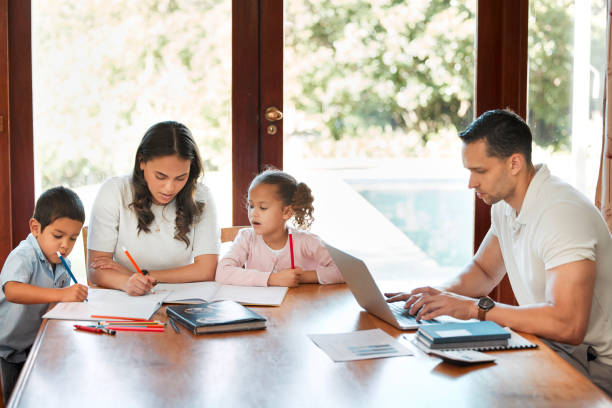 istock Young mixed race mother helping her children with homework while their father works on a laptop at a table in the lounge. Little siblings drawing together. Hispanic man typing emails 1398193318