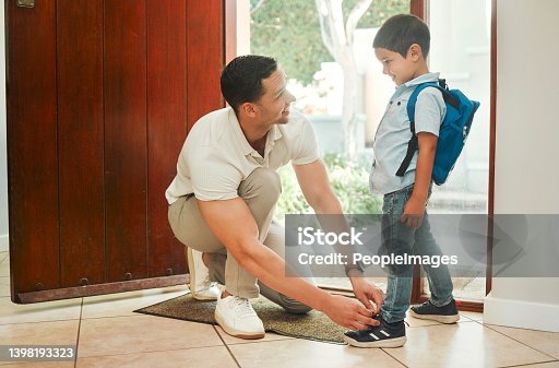istock Happy single father tying his son's shoelaces before school in the morning. Adorable mixed race little boy carrying a backpack and getting help from his single parent. Hispanic man and child at home 1398193323