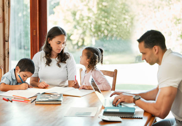 istock Young mixed race mother helping her children with homework while their father works on a laptop at a table in the lounge. Little siblings drawing together with their mom. Hispanic man typing emails 1398193324