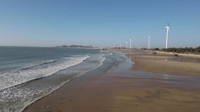 The sea, waves and wind turbines under the blue sky