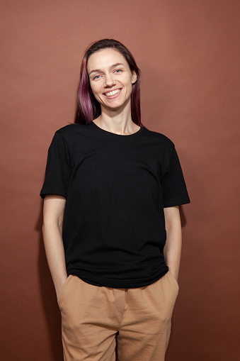 Studio portrait of a 30 year old woman with purple hair in a black t-shirt on a brown background