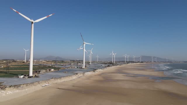 The coastline under the blue sky and the wind turbines on the beach