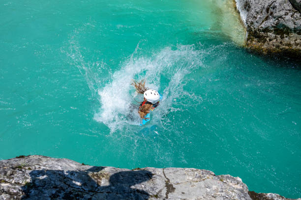 Woman jumping from rock. Splashing crystal clear cold water after hitting surface. Adrenaline sport in mountain nature. Amazing turquoise clear water in Soca river, Slovenia.