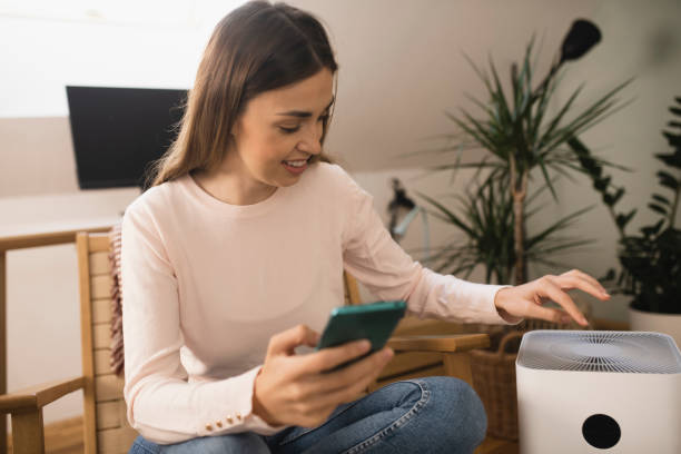 istock Happy young woman turning on air purifier using a smartphone 1398204242
