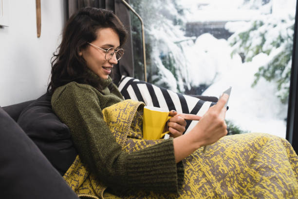 istock Happy young woman warming under the blanket and using tablet 1398204255