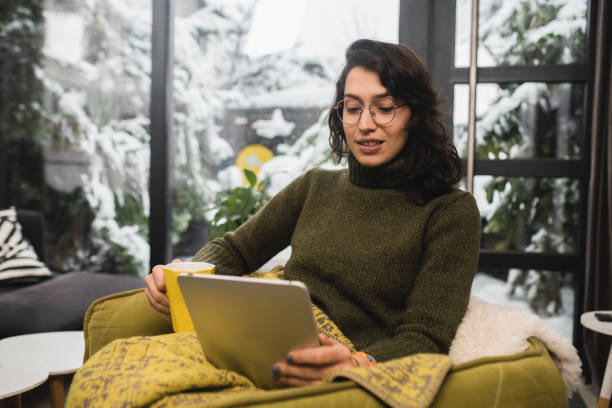 istock Happy young woman warming under the blanket and using tablet 1398204262