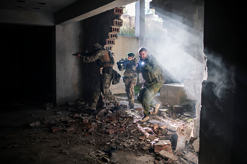 Soldiers with shotguns running through bombed building in war.