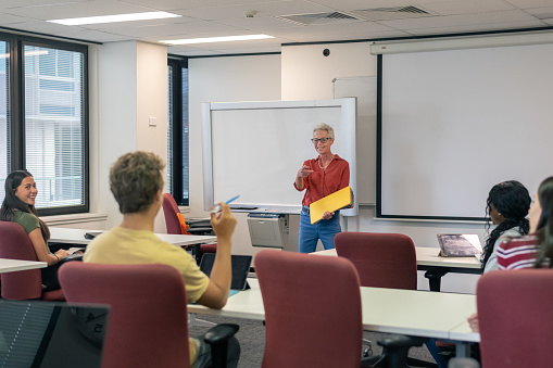 Mature adult woman teaching multiracial group of high school students in modern classroom.