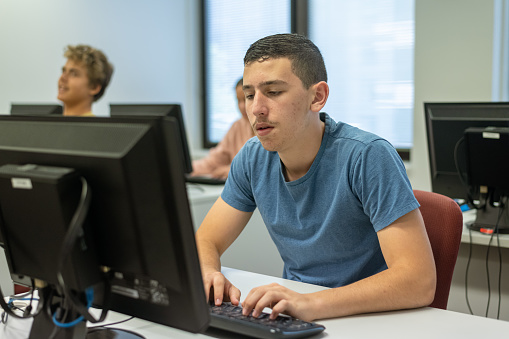 A male Caucasian teenager works on a computer while attending a coding class at his high school.