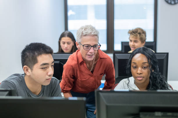 High school professor helping students with assignment in computer lab stock photo