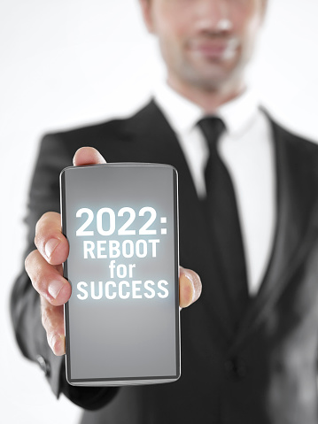 Businessman holding a mobile phone with ‘2022 reboot your success’ text  on the screen